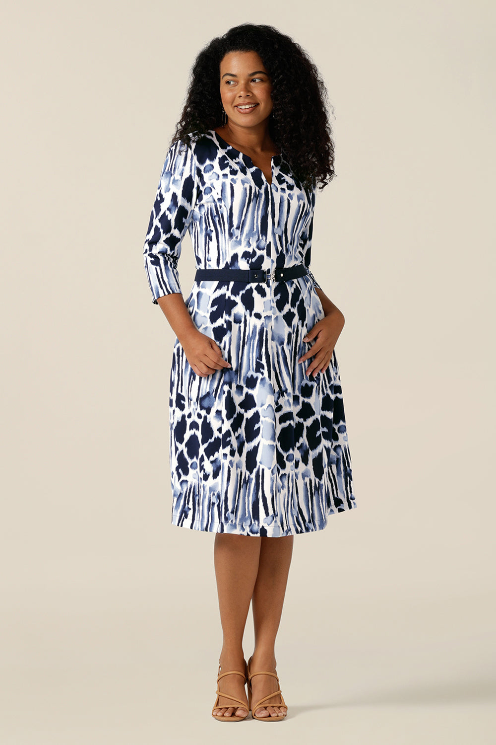 a woman wears a panelled work dress in navy and white jersey. The fitted jersey dress has a round neck with V opening, side pockets and below-the-knee length skirt. The waist of this comfortable size 12 shift dress is cinched with a navy stretch belt with silver buckle.