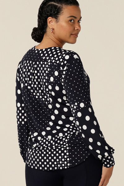 Back view of a size 12, curvy woman wearing a long sleeve, V-neck top in navy and white spot patterned jersey. Australian-made, wear this top as smart-casual wear for the office.