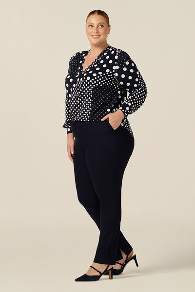 A size 18, fuller figure woman wears a long sleeve, V-neck top in navy and white polka dot print jersey. Made in Australia, by Australian and New Zealand women's clothing company L&F, this is a good top for workwear and casual wear.