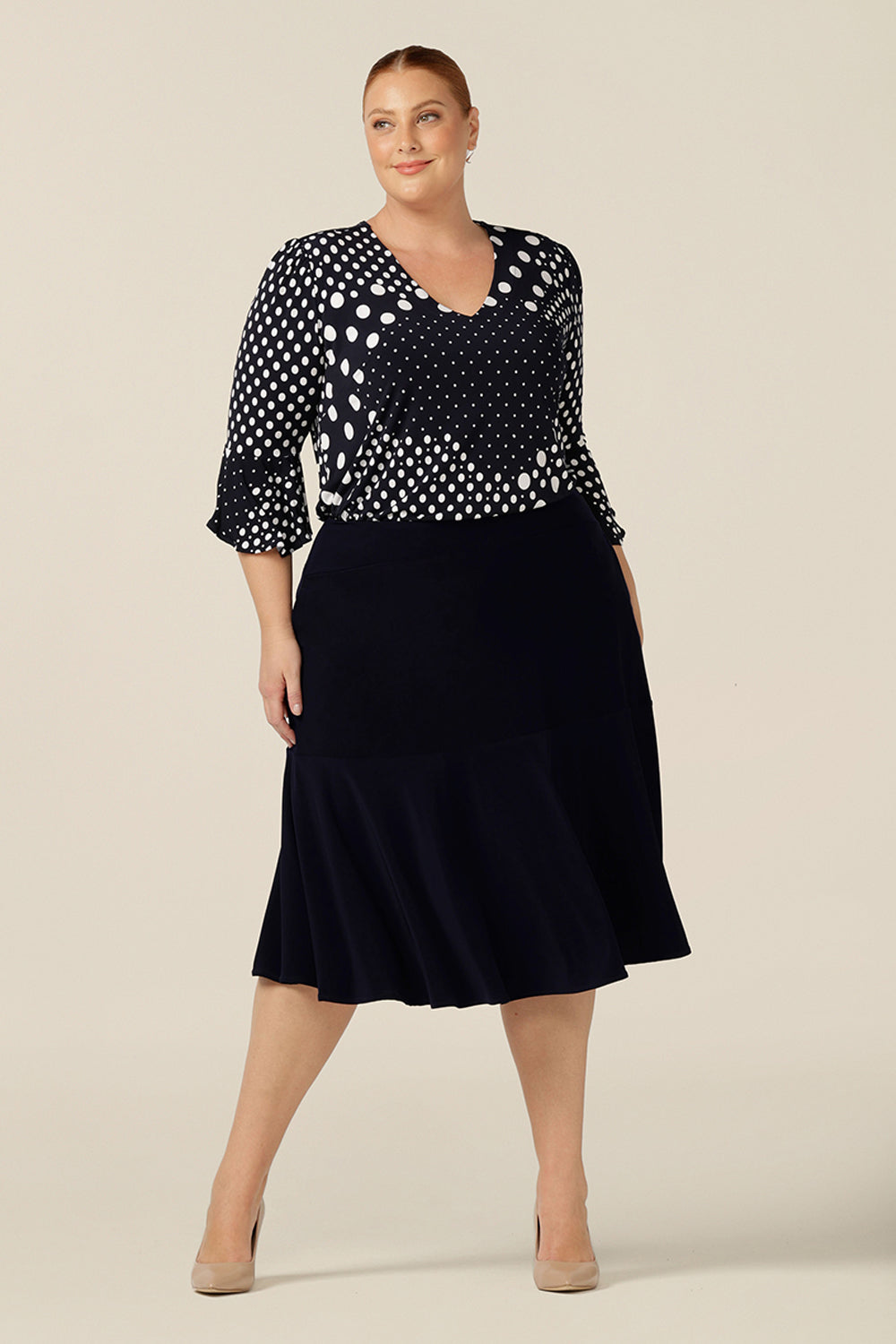 A chic top for plus size and fuller figure women, this V-neck top with fluted 3/4 sleeves comes in a navy and white polka dot print. Worn with a knee-length navy skirt, this top is good for work and corporate wear.