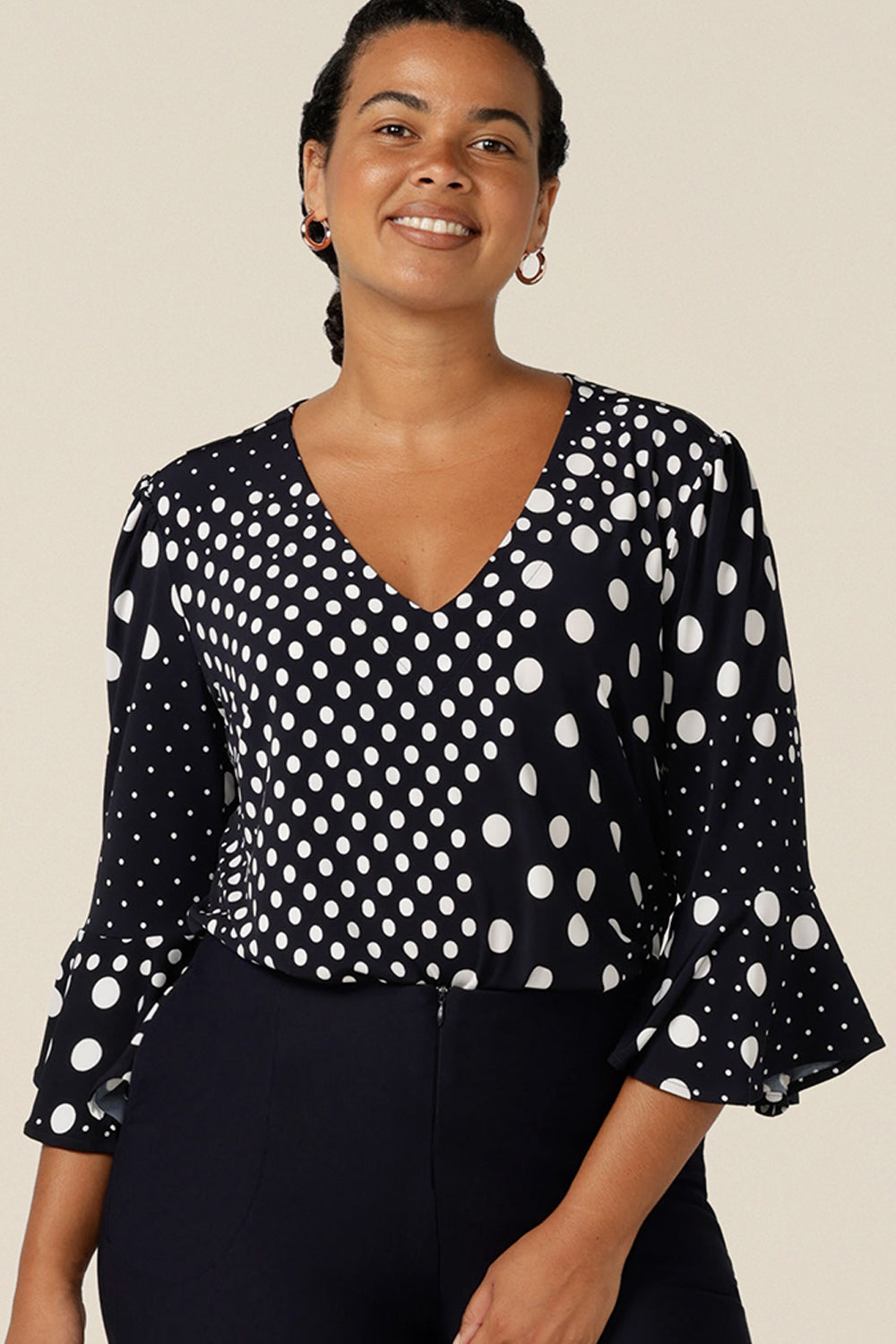 A women's workwear top in navy and white polka dot print. Featuring a V neckline and 3/4 sleeves with fluted cuffs, this top is made in Australia for petite to plus size women,