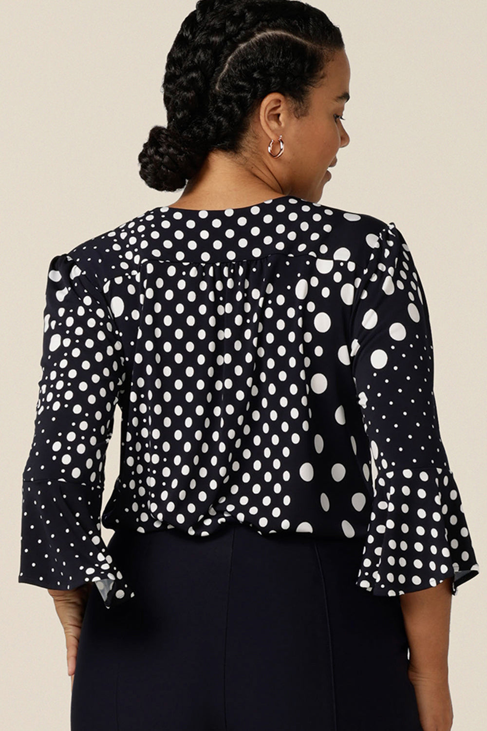 Back view of a women's work wear top in navy and white polka dot print. Featuring a V neckline and 3/4 sleeves with fluted cuffs, this jersey top is made in Australia for petite to plus size women,