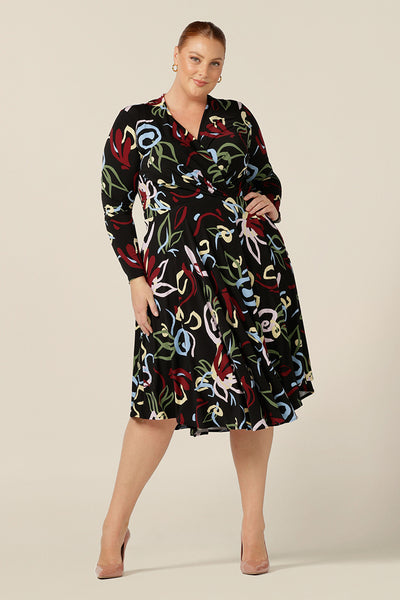 A size 18, fuller figure woman wears a knee length work dress with wrap-over bodice and full length sleeves made by Australian and New Zealand women's clothing brand, L&F.