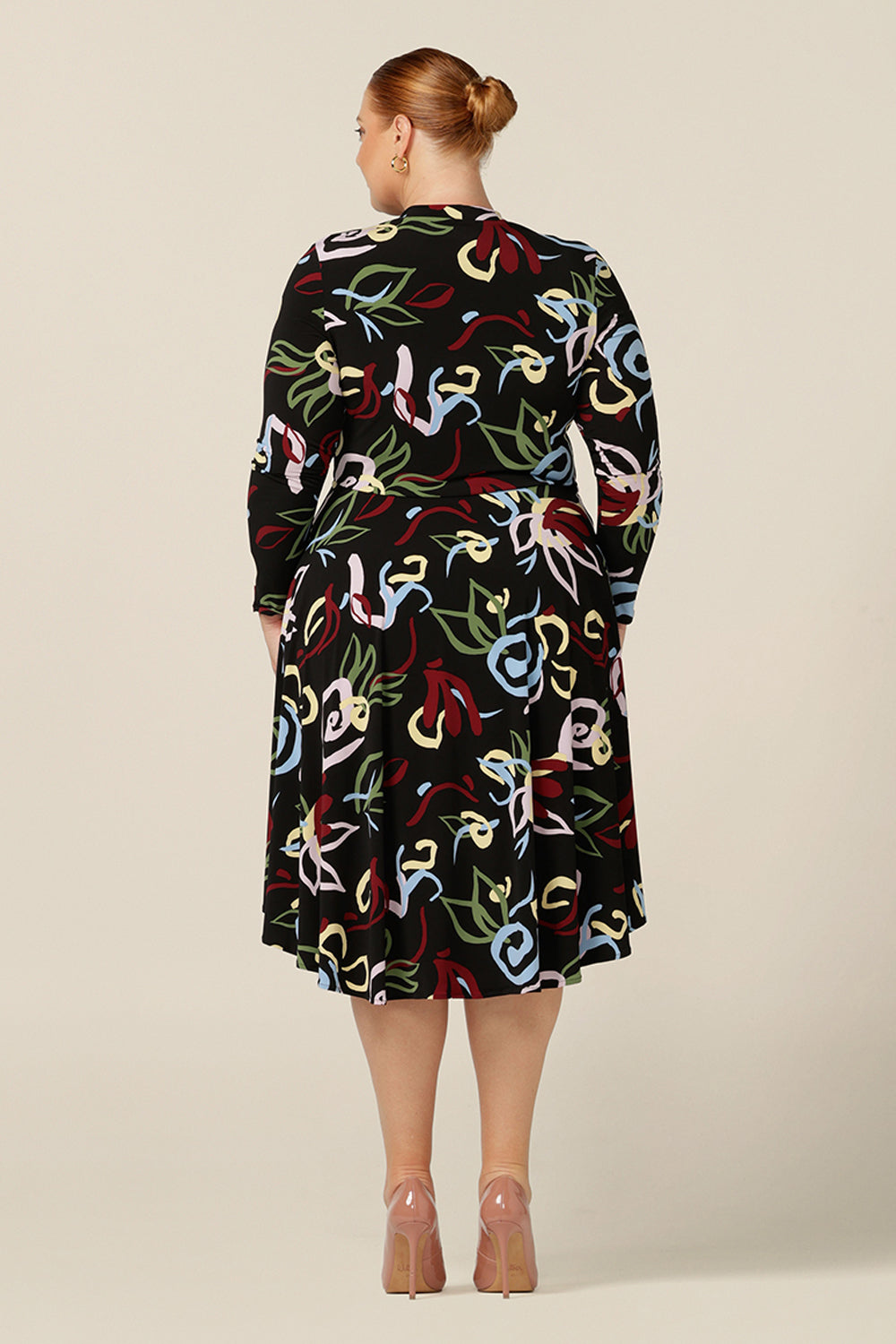 Back view of a plus size woman wearing a knee-length, jersey, work dress with long sleeves. In printed jersey, abstract patterns add colour to the black base of comfortable dress.