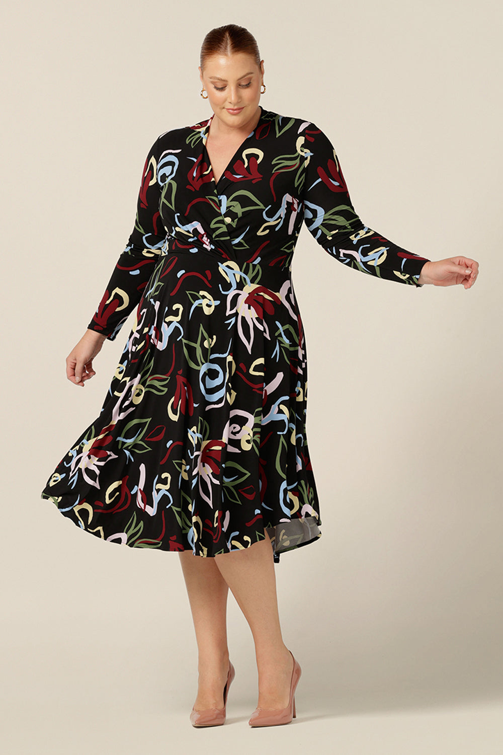 A size 18, plus size woman wears a knee length work dress with crossover bodice and full length sleeves made by Australian and New Zealand women's clothing label, Leina and Fleur..