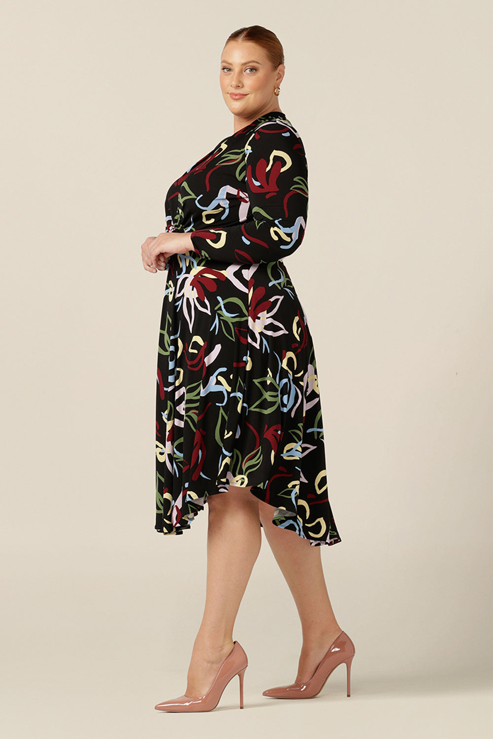 A size 18, curvy woman wears a knee length jersey dress with wrap-over bodice and full length sleeves, made in Australia by women's clothing brand, L&F.