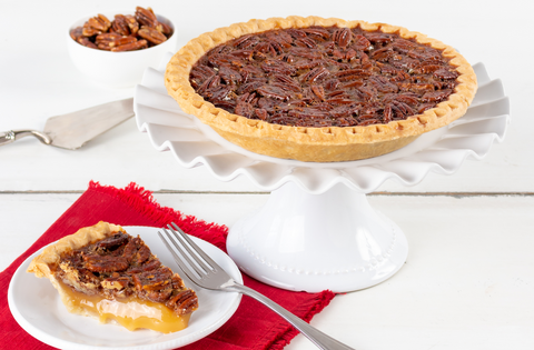 a Pecan Pie atop a white cake stand next to a gooey slice of the same on a white plate. 
