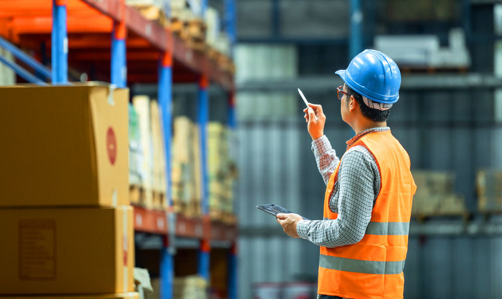 Person in worker vest taking inventory and pointing at products on warehouse shelves