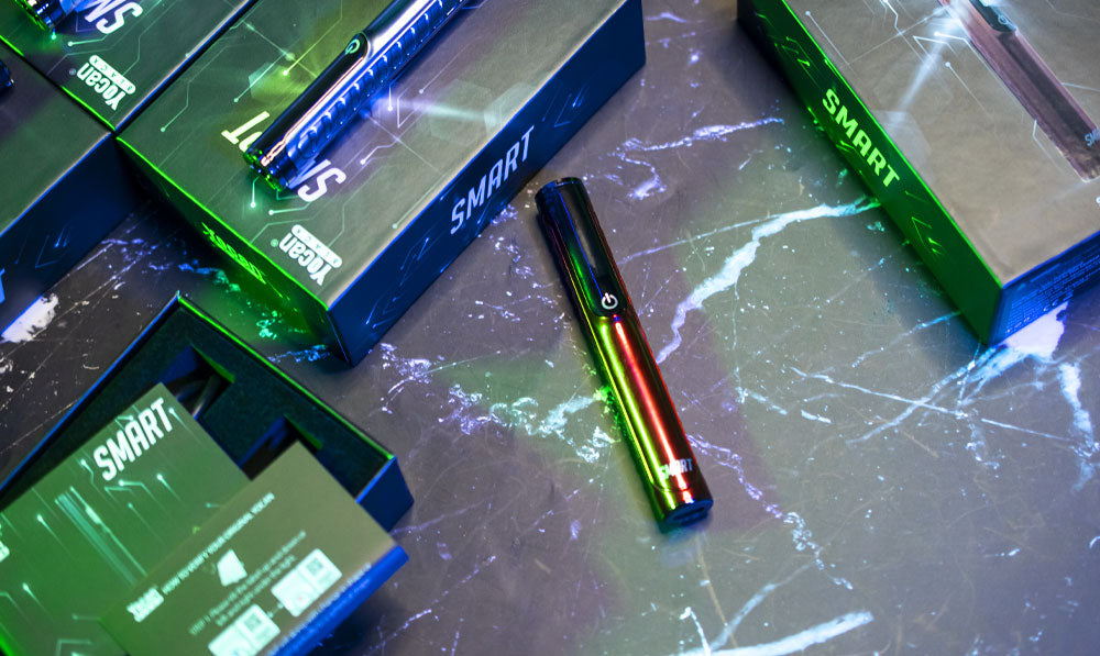 Yocan Black Smart cartridge vaporizers resting on lightning surface with packaging nearby and soft green lighting