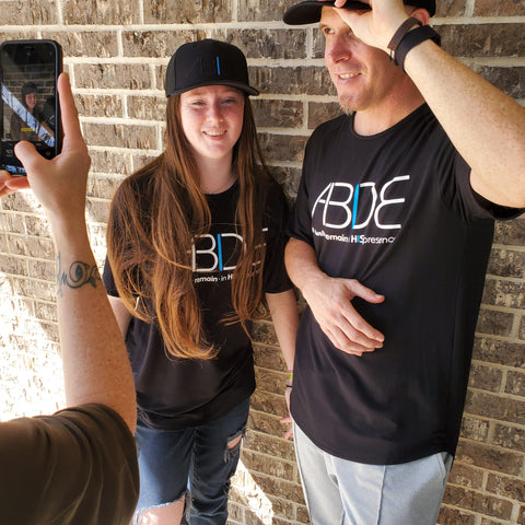 Fotografía de papá e hija con camisetas de bambú negras y gorras de camionero