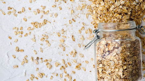 A jar of oats on the right spilled all over on a blank surface. 
