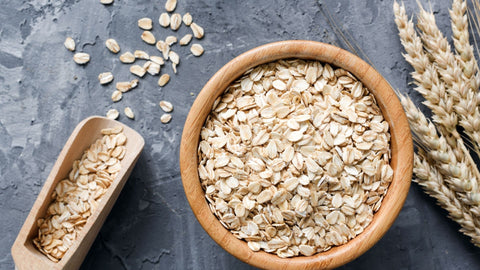 A bowl of oats, with wheat to the right and a spoon of oats to the left. 