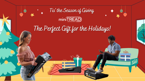 woman smiling holding carrying a miniTREAD from the christmas tree to a the couch where a black man is sitting looking at the miniTREAD remote with the miniTREAD under his feet in front of the couch.