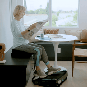 Woman sitting at her kitchen table reading the papaer and walking while seated with miniTREAD