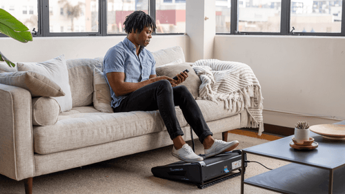 Young man sitting on couch using miniTREAD and looking at his workout metrics