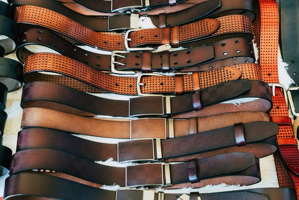 Various types of brown leather belt in a row for display and sale on the market.