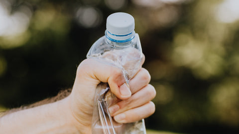 Male crushing plastic water bottle in park