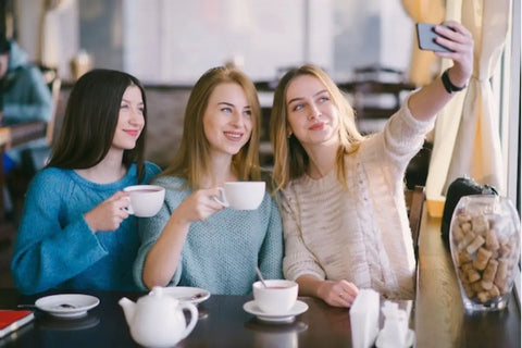 tiga orang teman yang sedang nongkrong di cafe sambil foto-foto