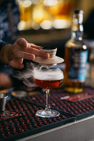 Smoked Cocktail with Cocktail smoker being lifted off cocktail with smoke in glass