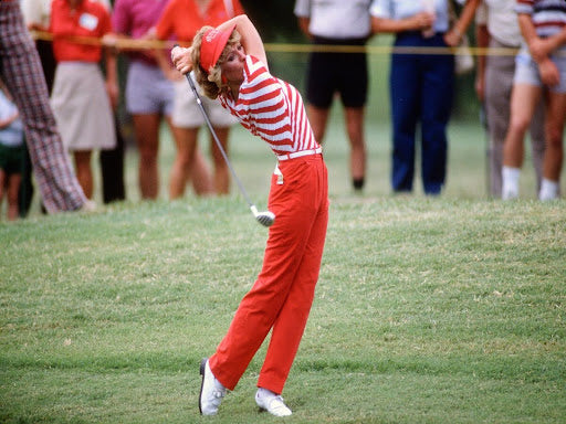 White female golfer in mid-swing | orange and white pantsuit | orange visor | golf event