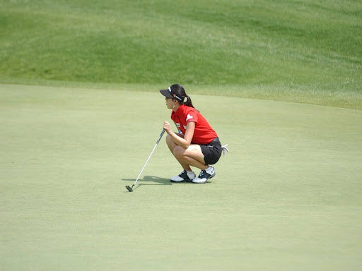 Asian female golfer crouching | black visor | green field | golf putt