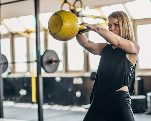 Blonde-haired woman swinging a yellow kettlebell
