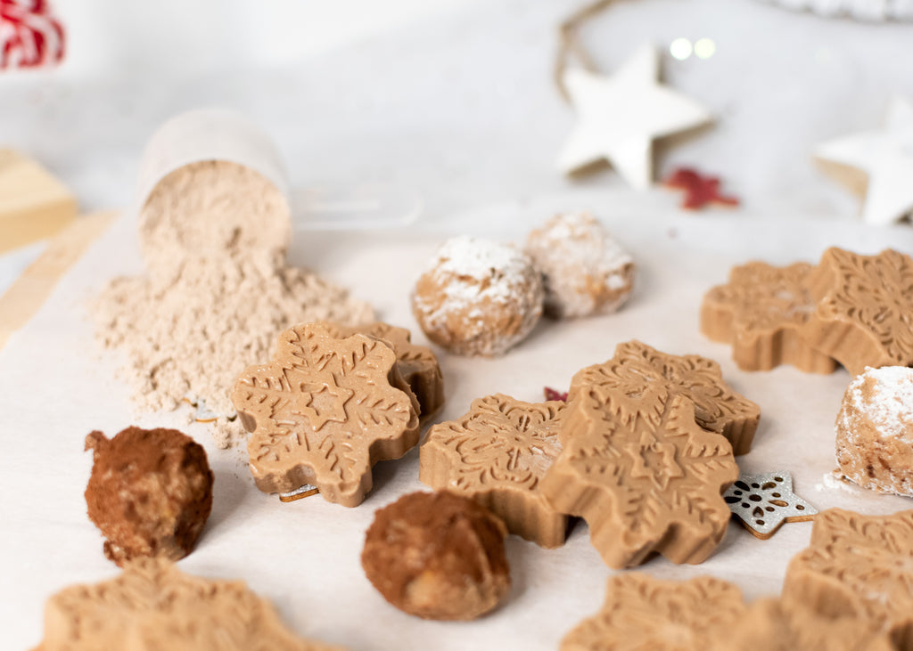 protein powder fat bombs made with pounamu protein powder and molded into the shape of snowflakes and snowballs, arranged next to a protein powder scoop and Christmas decorations