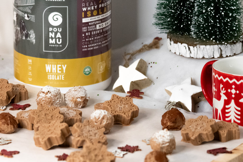 Fat bombs shaped like snowflakes and snowballs with a tub of pounamu protein chocolate whey isolate in the background with Christmas decorations