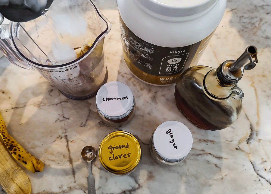 All ingredients used for gingerbread protein shake sitting on a marble countertop. 