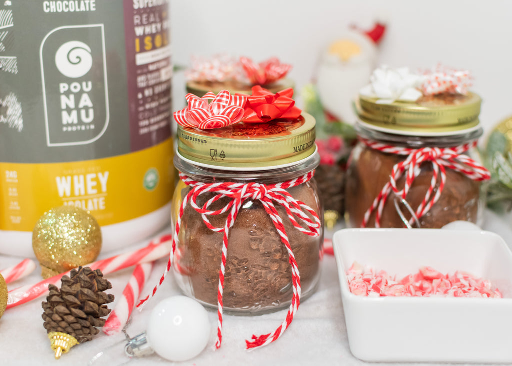 Pounamu Protein Hot Chocolate Mix in holiday jars with holiday decorations and a tub of Pounamu Protein Powder displayed together