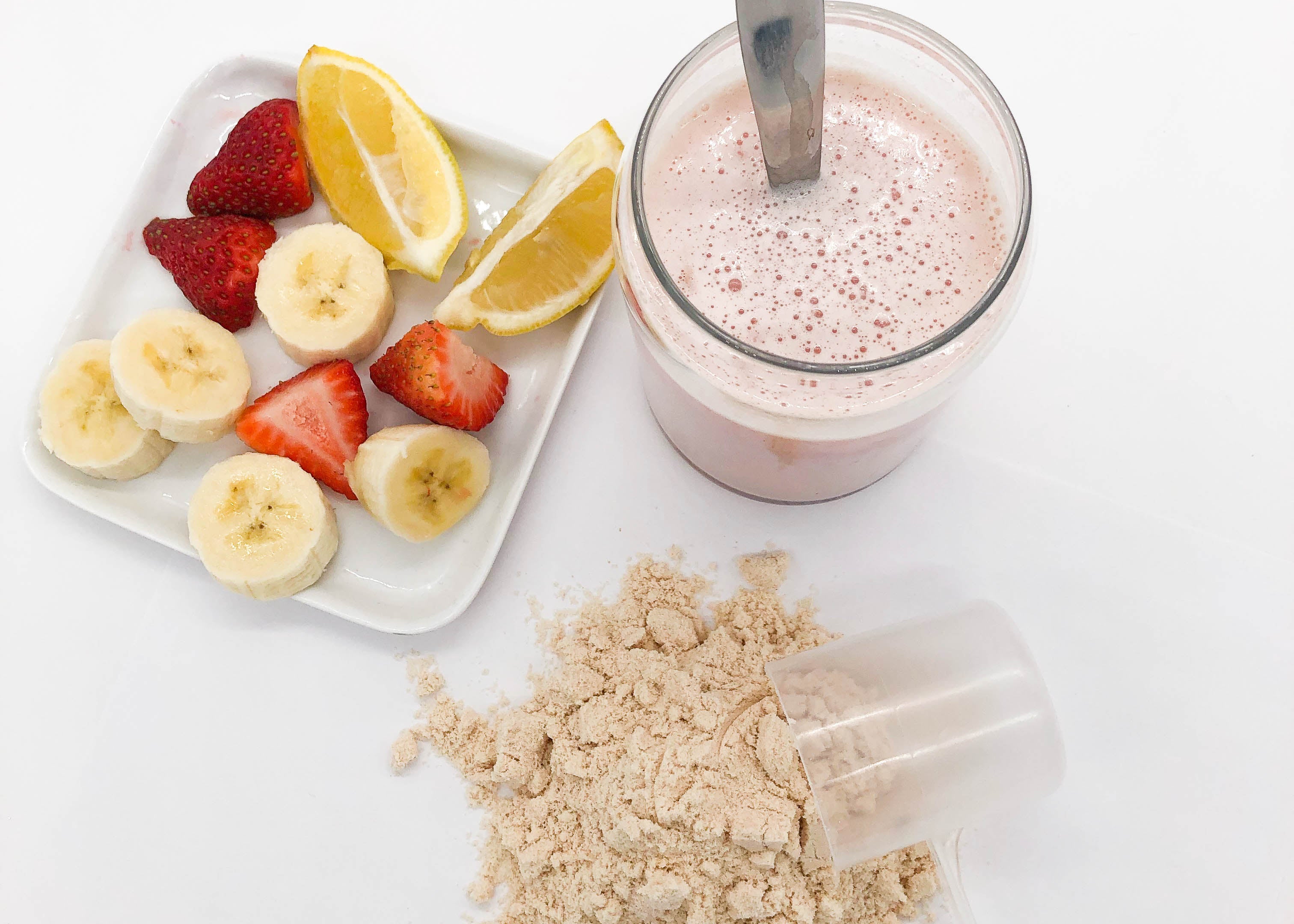 A scoop of Pounamu Protein Recovery Blend powder, a glass of Recovery blend powder mixed with water and a white square plate with cut lemon, strawberries and bananas on it.