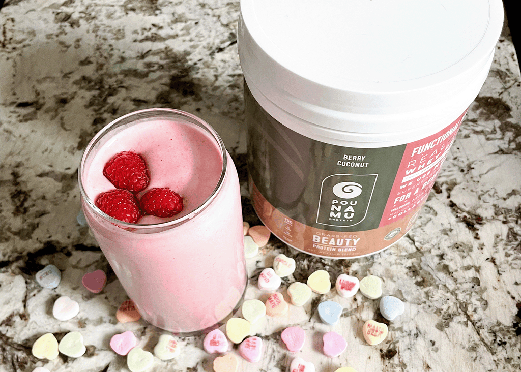 Pink valentines smoothie with raspberries on top and candy hearts on the counter. 