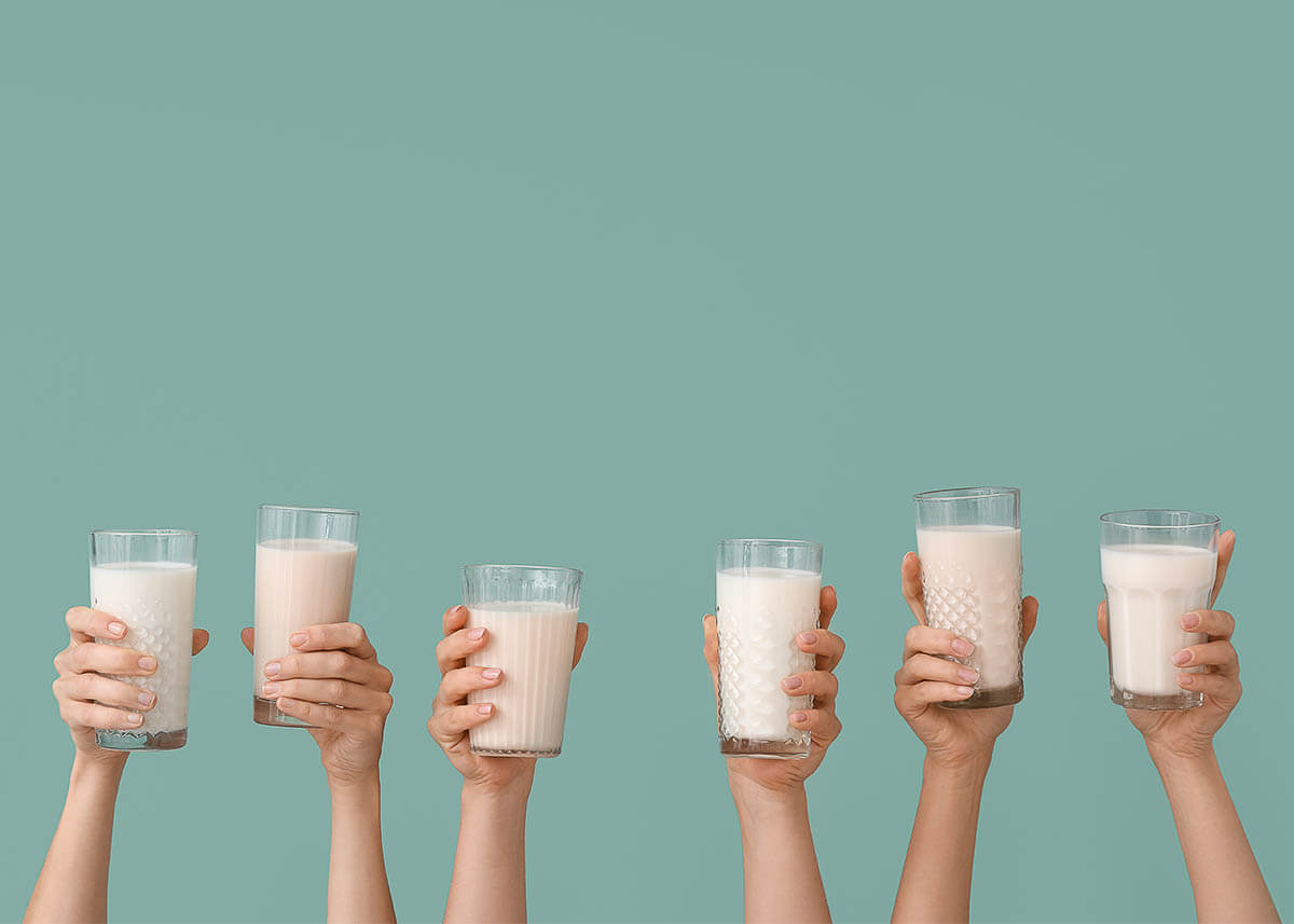 Six hands holding six glasses of milk in the air with a turquoise background.