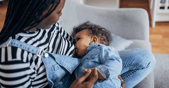 A mother breastfeeds her baby while sitting on a couch at home.