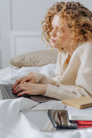 woman in bed typing on laptop keyboard
