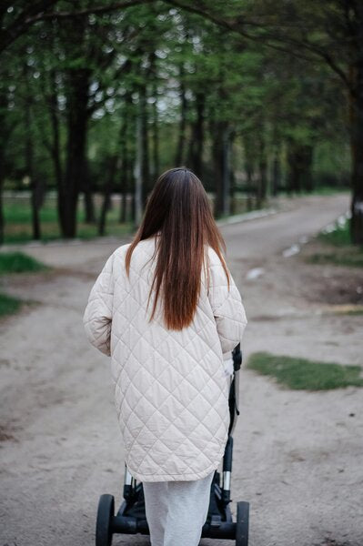 Une femme de dos en dépression postpartum marche en nature avec sa poussette.