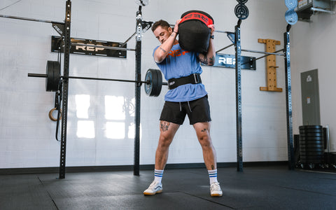 A man wearing a nylon lifting belt lifting a sandbag
