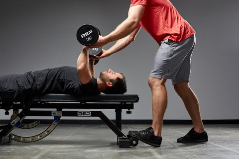 Man spotting friend doing dumbbell bench presses