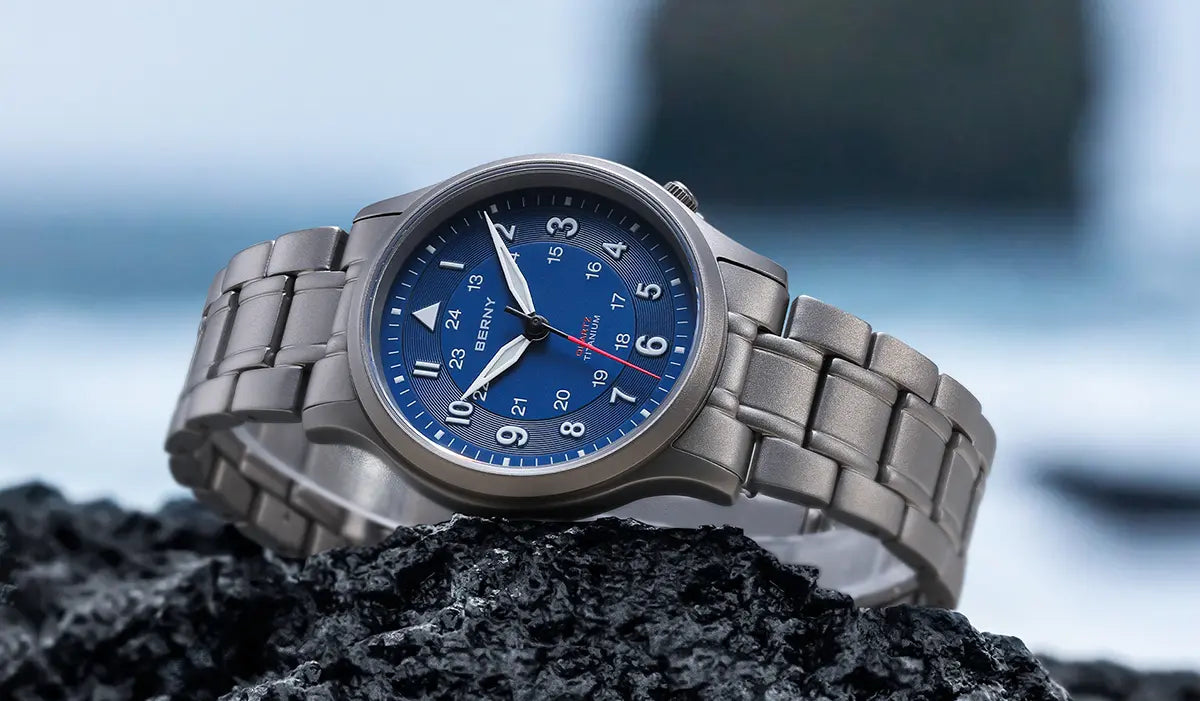 Die Berny Uhr thront kunstvoll auf einer felsigen Oberfläche und besticht durch ein Titanarmband und ein markantes blaues Zifferblatt. Ihr Design vereint Eleganz und Robustheit und eignet sich sowohl für abenteuerliche als auch für formelle Anlässe. Diese vielseitige Uhr verbindet Funktionalität mit einer markanten Ästhetik.