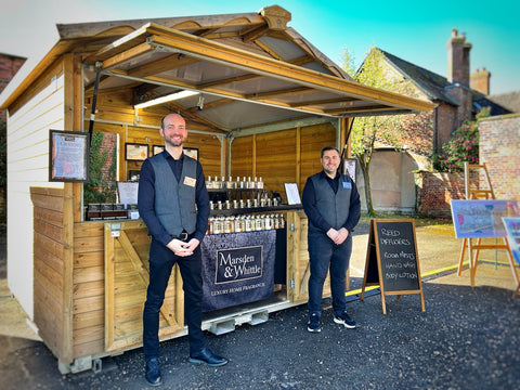 Scott and Matt standing outside a wooden chalet with the Marsden & Whittle stall in the background.