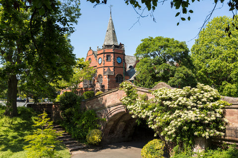 A photo of the dell in Port Sunlight with a red brick building in the centre and green trees either side in full bloom.