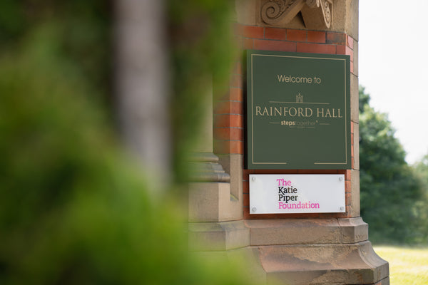 The new signage at Rainford Hall showing the Steps Together and The Katie Piper Foundations name plaques side-by-side, mounted to the red brick building.