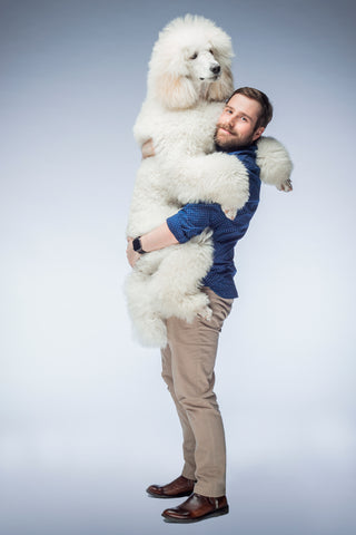 hombre sostiene en brazos a perro caniche gigante