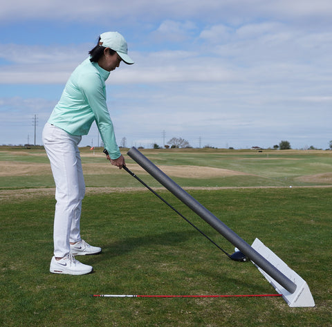 Golfer at setup with driver swinging under alignment stick to work on over the top move.