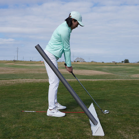 Golfer with iron at setup with Golf Boks holding up an alignment stick to work on swing plane and an inside takeaway.