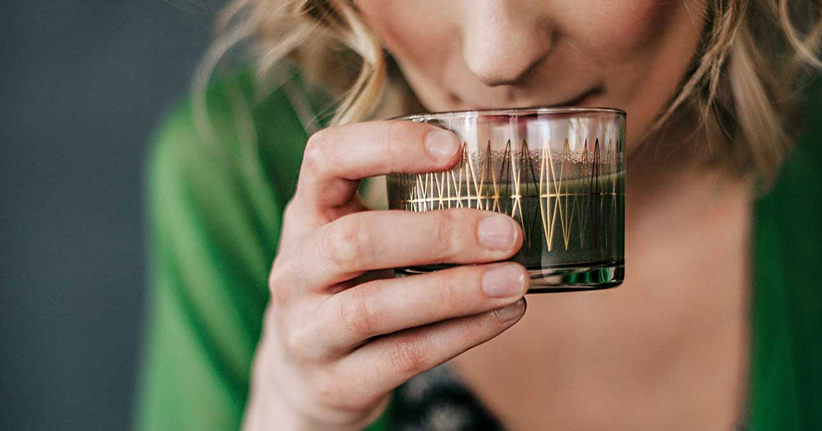 Woman drinking chlorophyll from glass