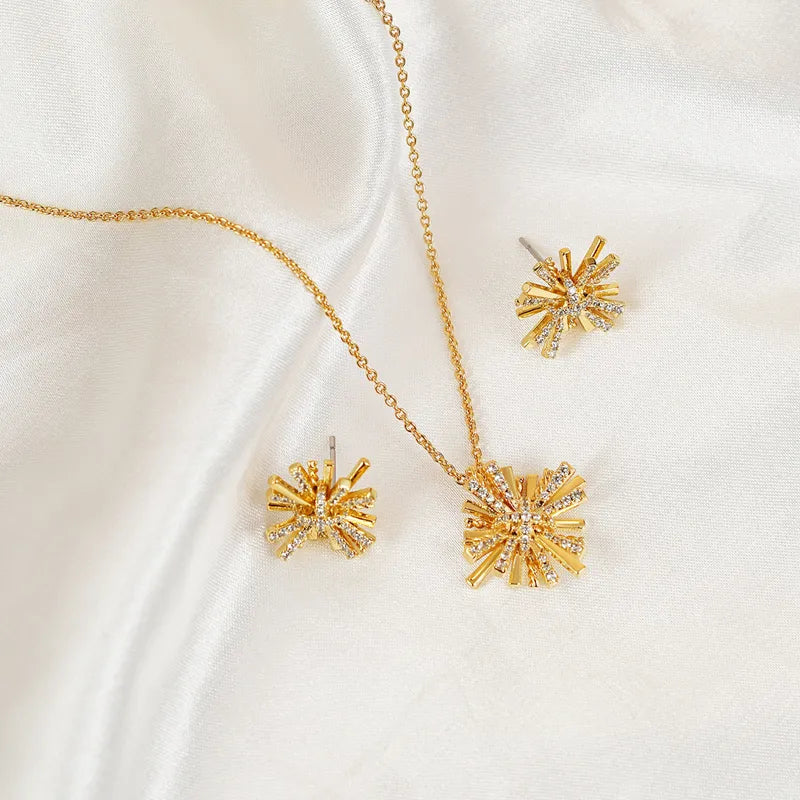 Close-up of gold-plated starburst earrings and necklace set displayed on a white cloth.