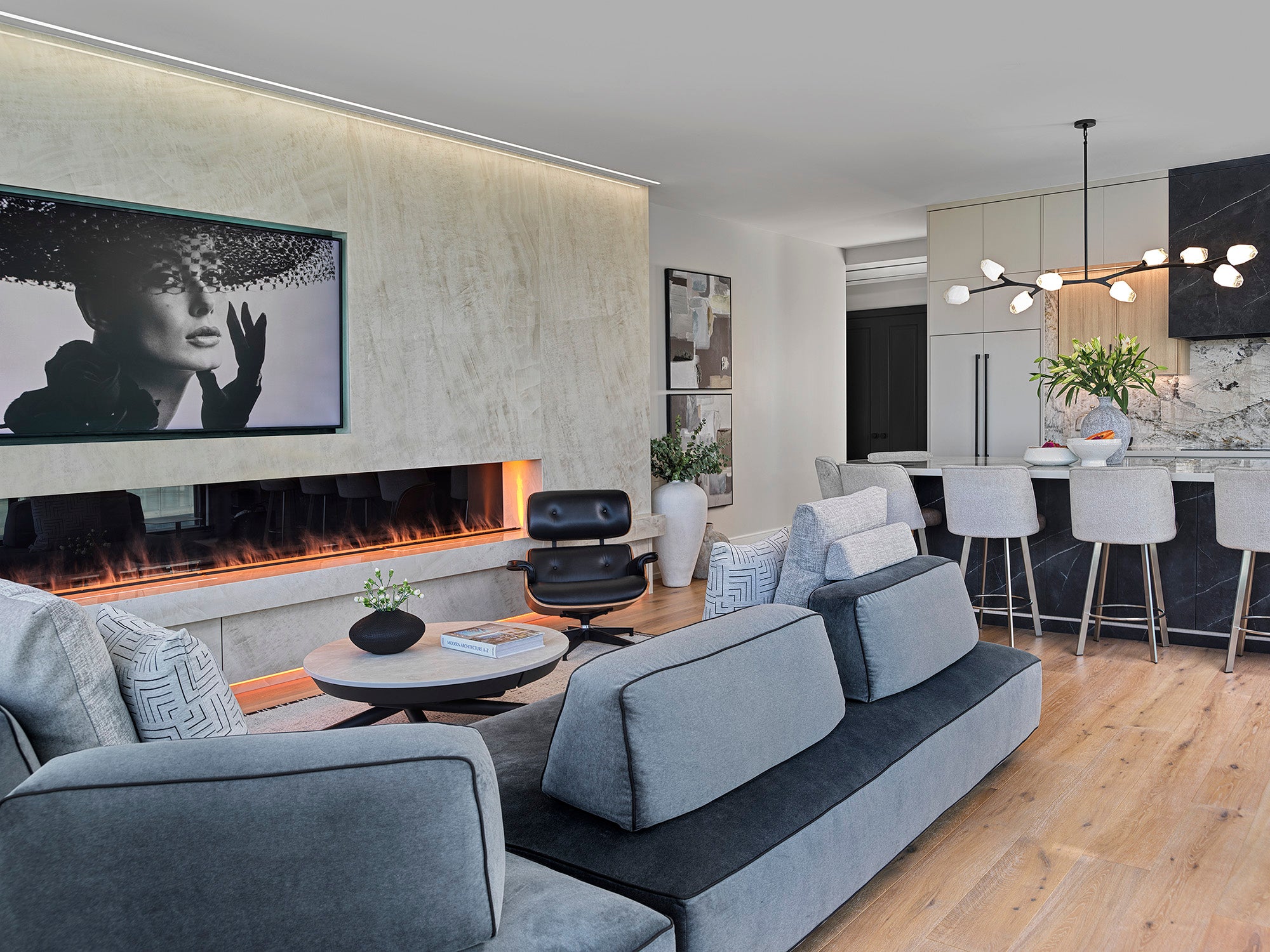 An elegant open-concept living space featuring the Flex Sectional, Flex Side Tables, and Soleil coffee table, complemented by a modern fireplace, bar seating, and a marble kitchen island, with sleek finishes and contemporary lighting.