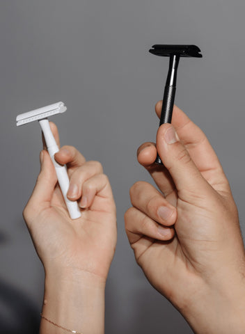 Two hands holding (left) white safety razor and (right) black safety razor