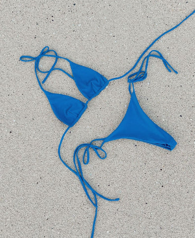 Flat lay of blue string bikini on sand